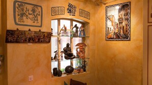 A room with a mural, a window with shelves displaying figurines, and a framed picture of a street scene. - Hotel Blume (Interlaken)