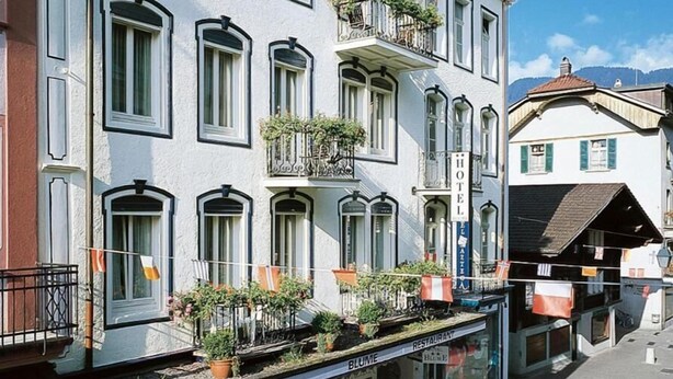 A hotel with multiple balconies, outdoor seating, and a storefront with a restaurant. - Hotel Blume (Interlaken)