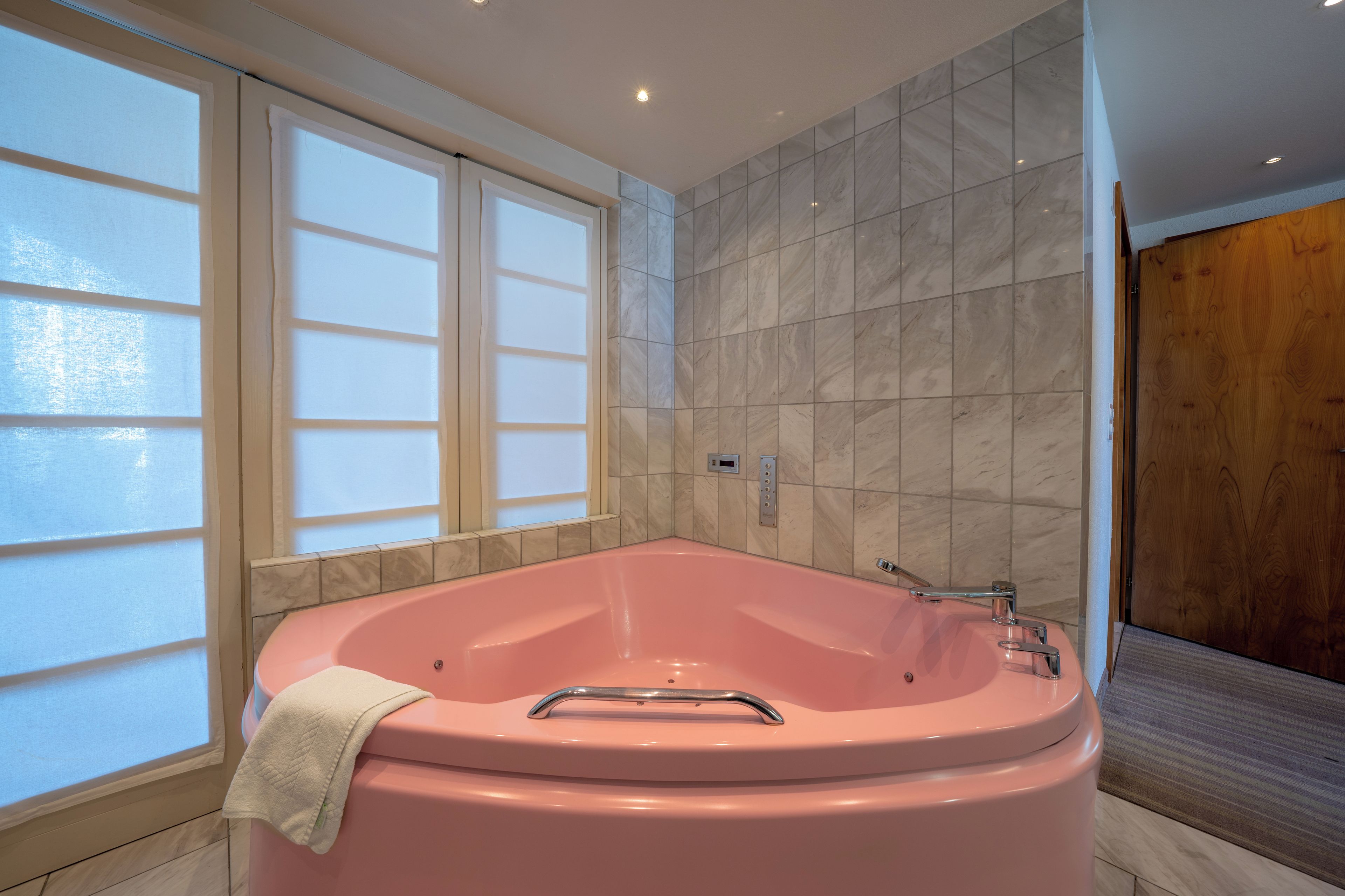 Une salle de bain moderne avec un grand jacuzzi rose, des fenêtres en verre dépoli et des carreaux de marbre.