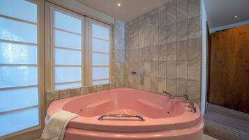 Une salle de bain moderne avec un grand jacuzzi rose, des fenêtres en verre dépoli et des carreaux de marbre.