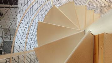 Eine Wendeltreppe mit Drahtgeflecht-Geländer, Holzhandläufen und beigefarbenen Stufen.