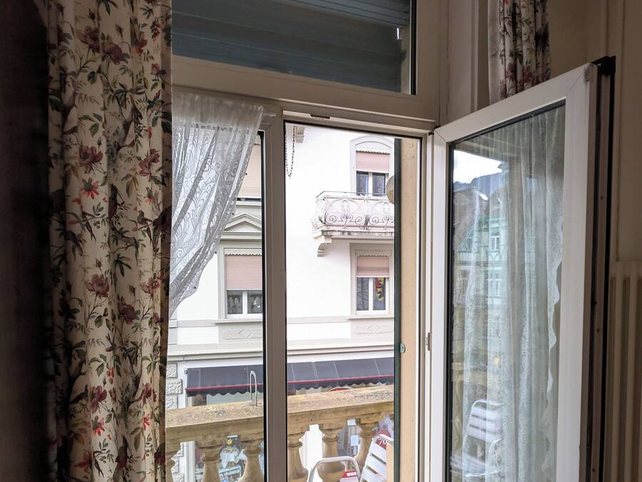 A room with a sliding glass door leading to an outdoor balcony. The balcony has a metal chair and a small table.