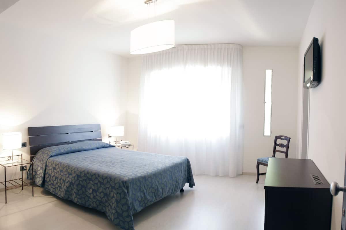 A bedroom with a bed, bedside tables, a desk, and a chair.