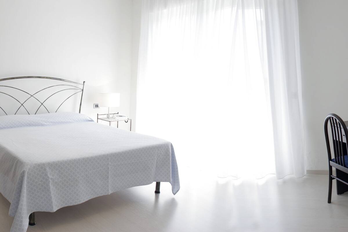 A bedroom with a bed, bedside tables, a desk, a chair, a TV, and a window with curtains.