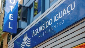 A hotel with a prominent sign reading 'ÁGUAS DO IGUÁÇU HOTEL CENTRO' and a visible entrance with a green sign indicating a card payment option.
