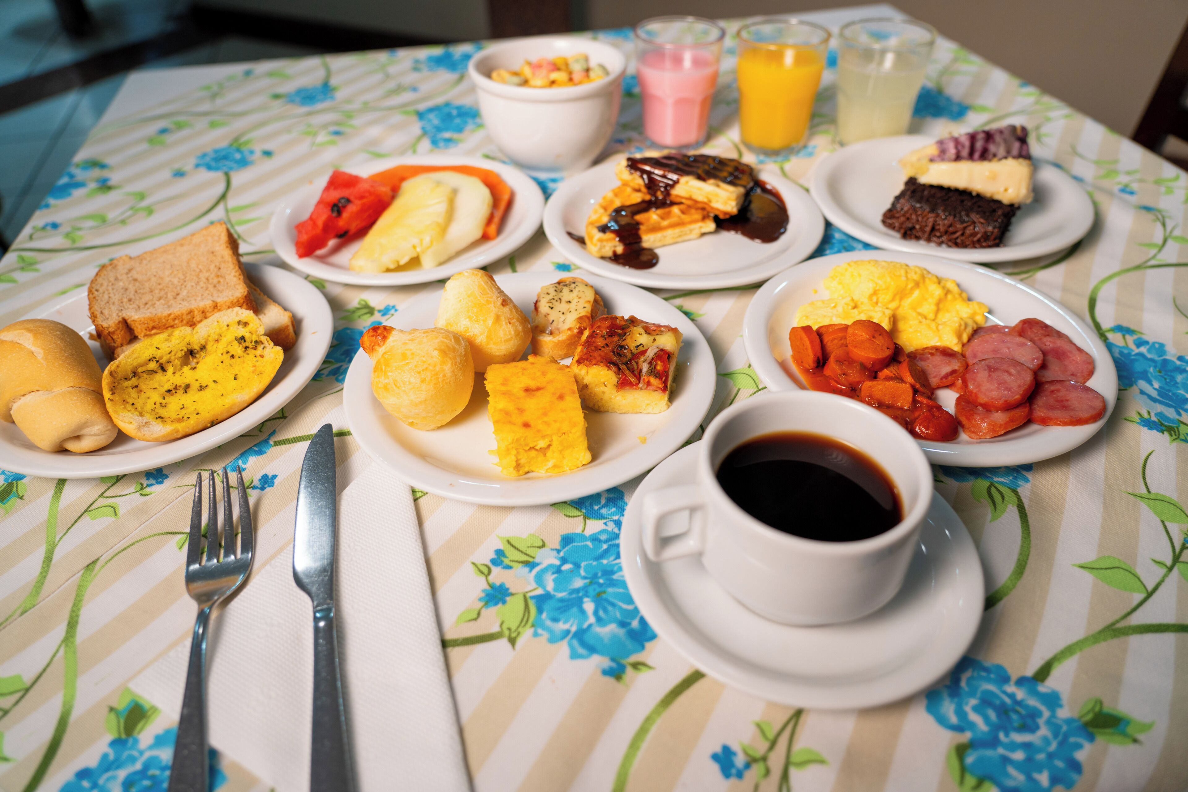 Una mesa de desayuno con platos de comida, una taza de café y un mantel con motivos florales.