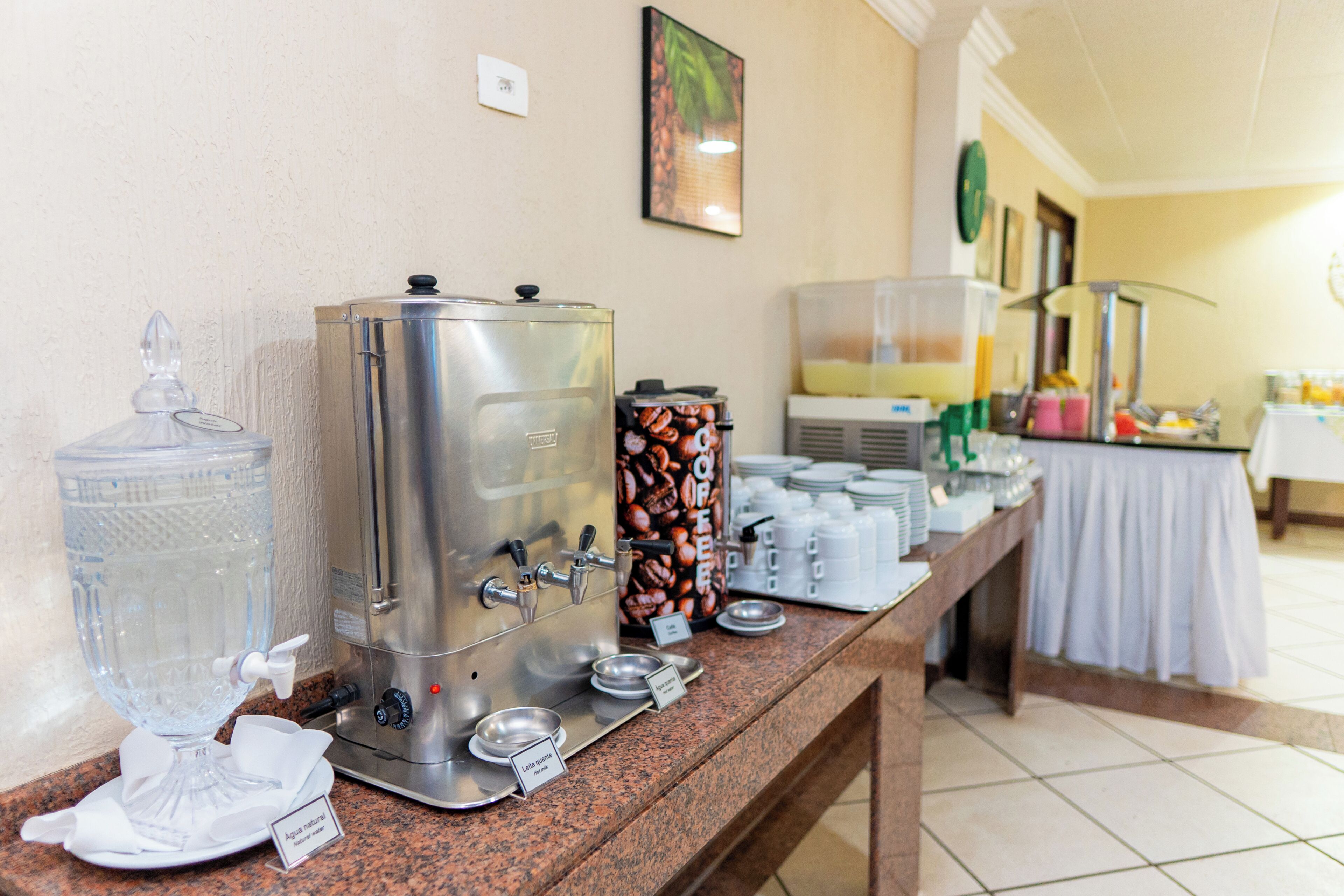 Un buffet avec un espace dédié au café, un distributeur d’eau et divers récipients contenant de la nourriture, le tout disposé sur un comptoir.