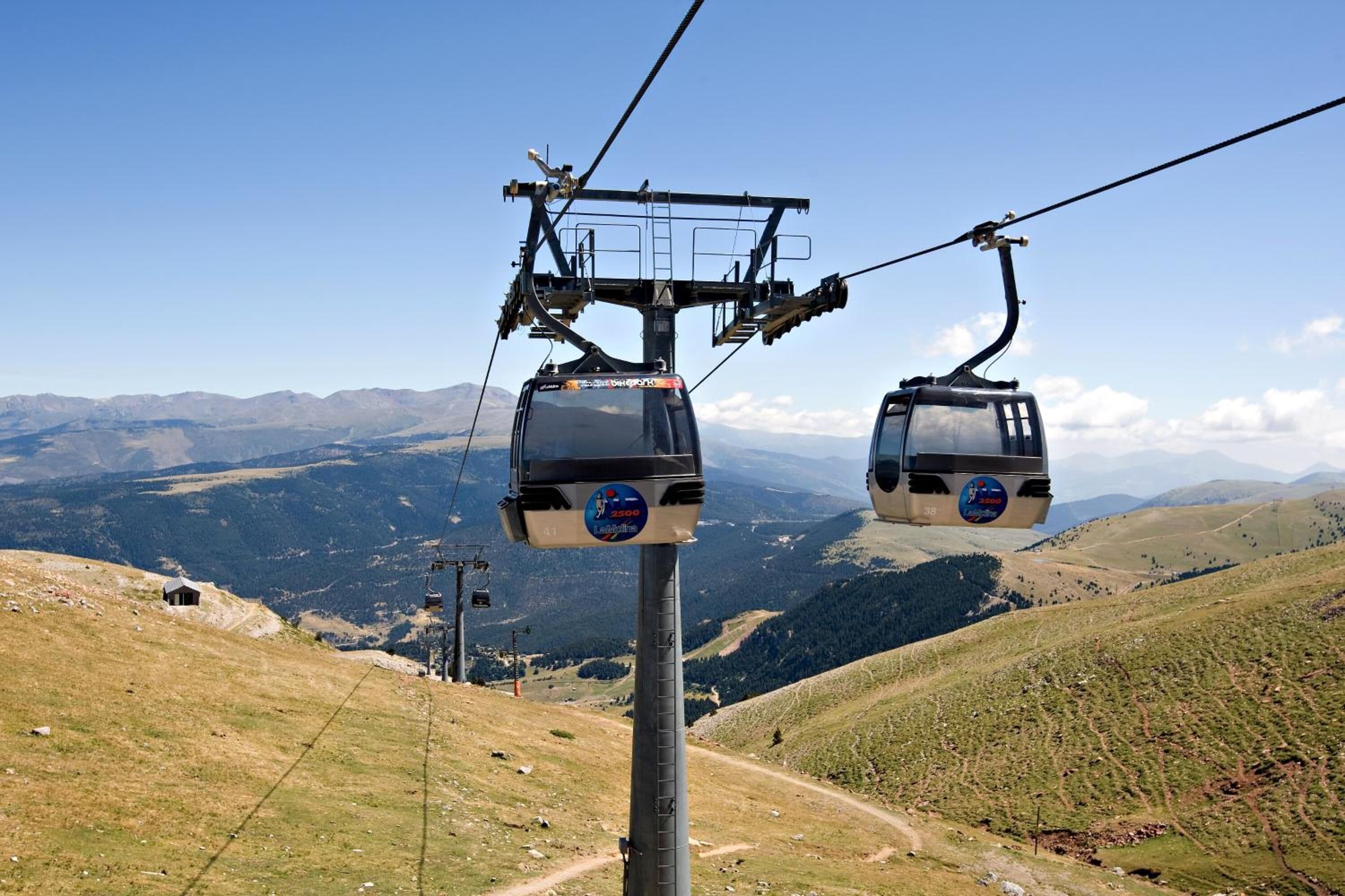 A cable car system with two gondolas, a clear sky, and a mountainous landscape in the background.