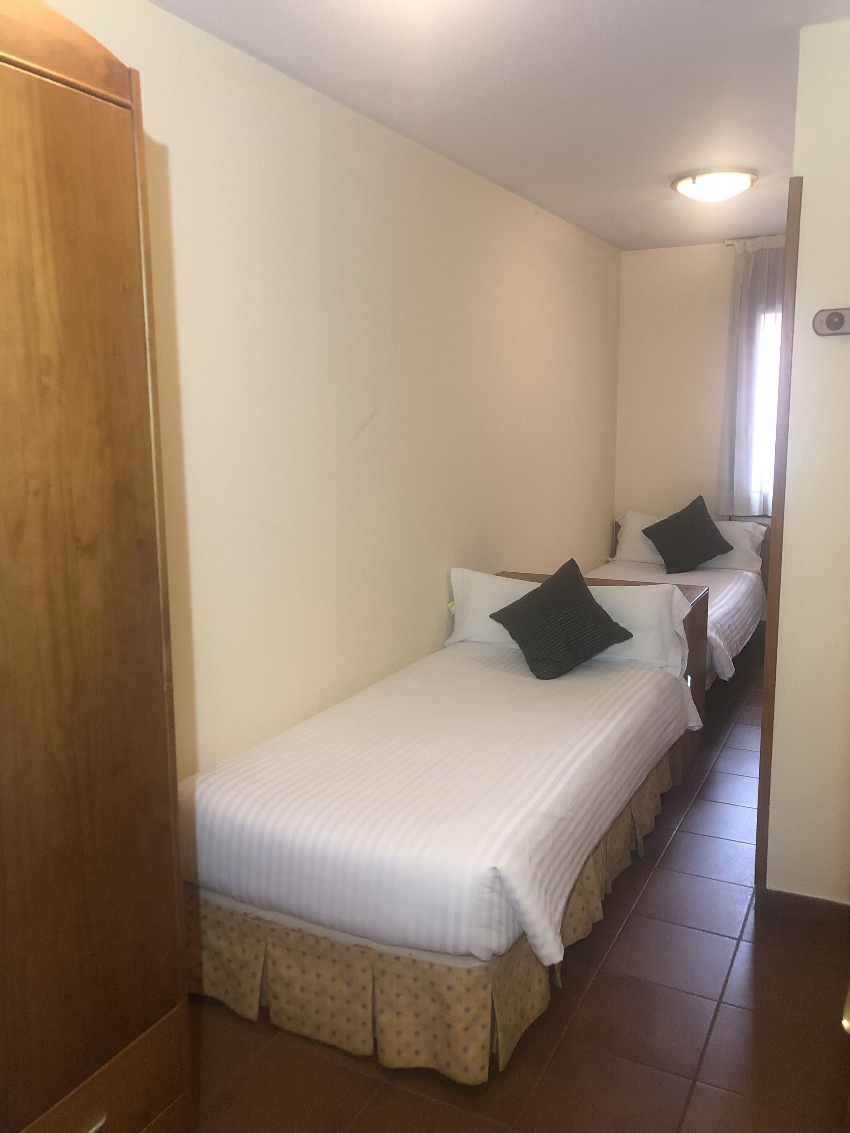 A hotel room with two single beds, a wooden wardrobe, and a tiled floor.