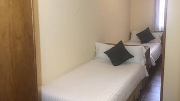 A hotel room with two single beds, a wooden wardrobe, and a tiled floor.