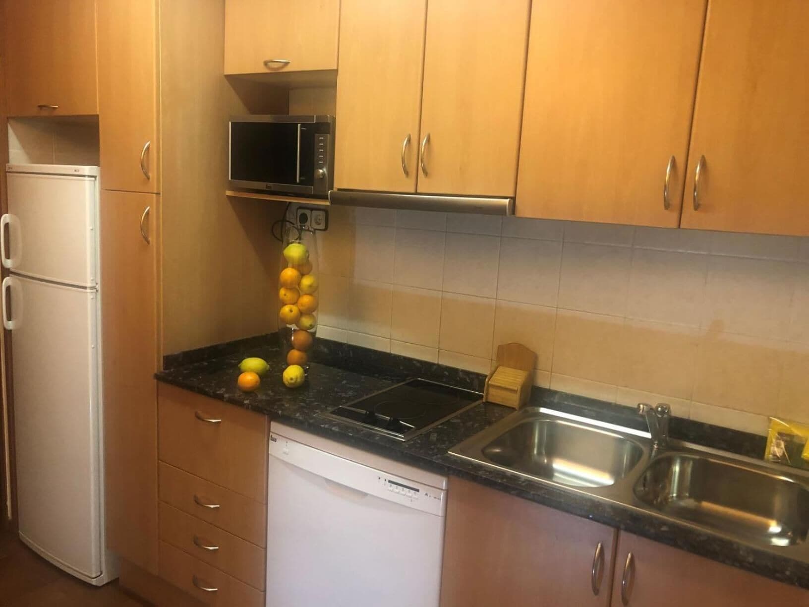 Una cocina compacta con armarios de madera, un refrigerador blanco, un microondas, un lavavajillas y un fregadero.