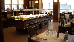 Zona de buffet amb una varietat d'aliments i una barra de servei ràpid. Taules preparades amb coberts i gots.