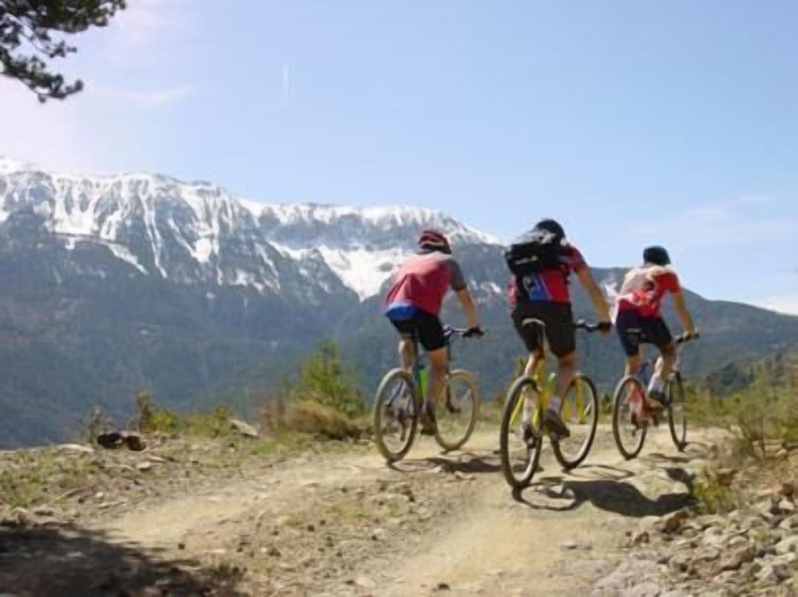 Tres ciclistas en un sendero de montaña con un pico nevado al fondo.