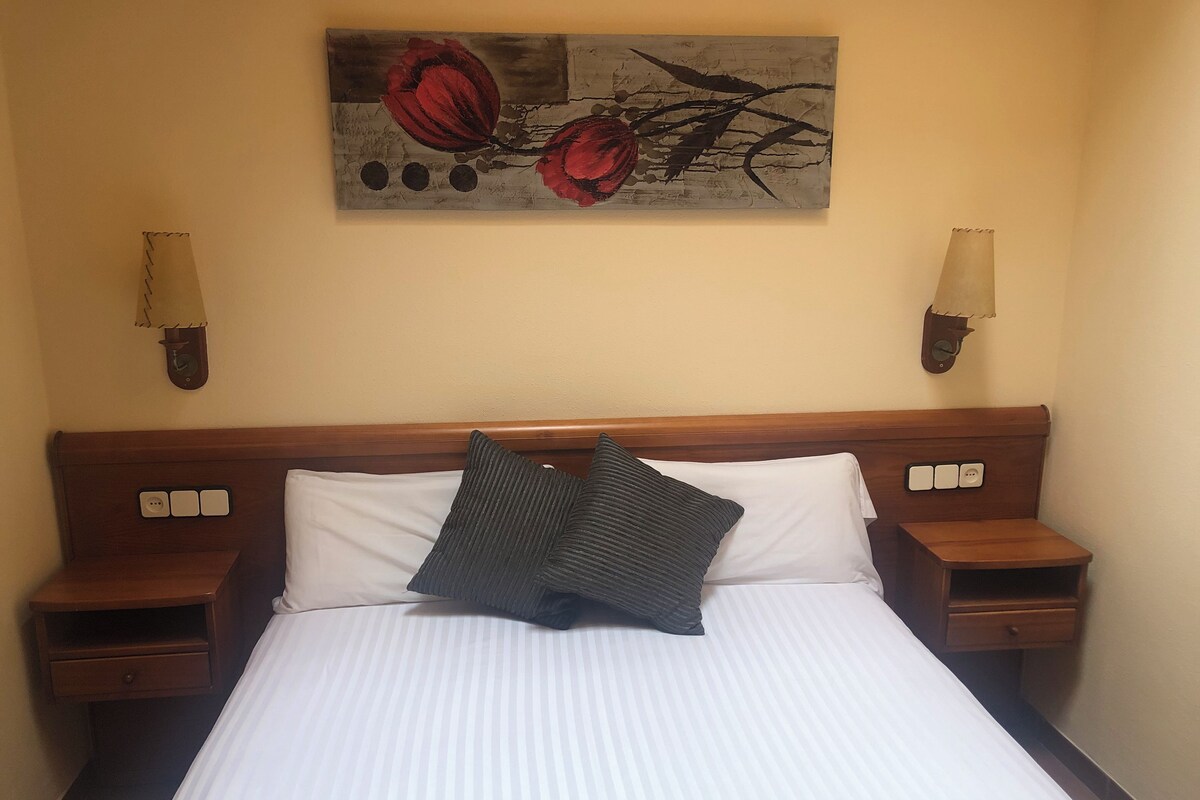 Ein Hotelzimmer mit einem großen Bett, zwei Nachttischen, einer Wandlampe und einem Gemälde über dem Bett.