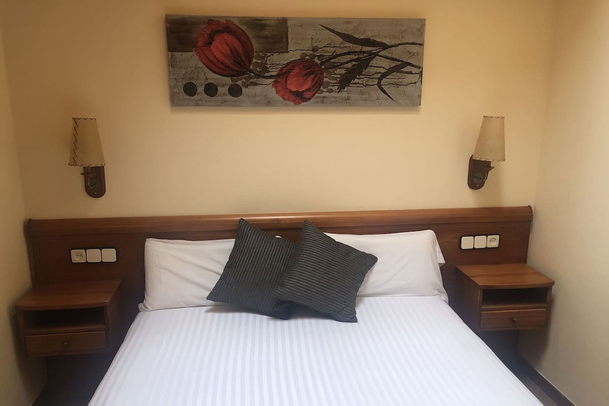 A hotel room with a bed, two bedside tables, a wall-mounted lamp, and a painting.
