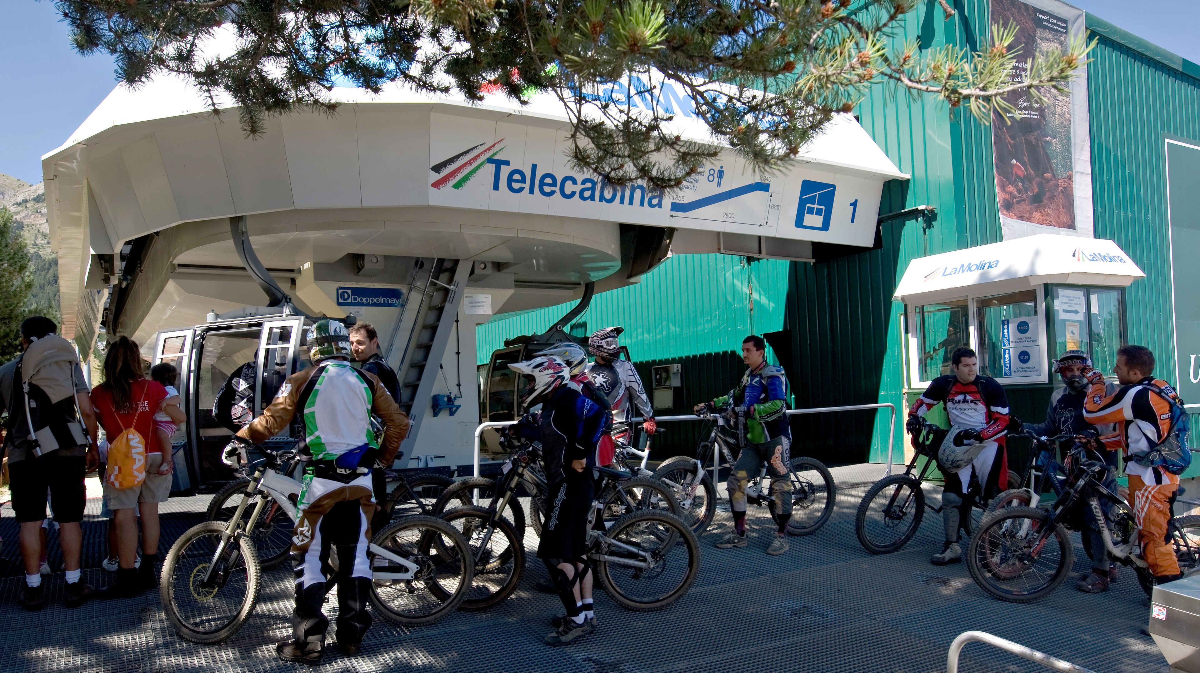 Un grupo de ciclistas reunidos cerca de un edificio con un letrero que dice 'Telecabina'.
