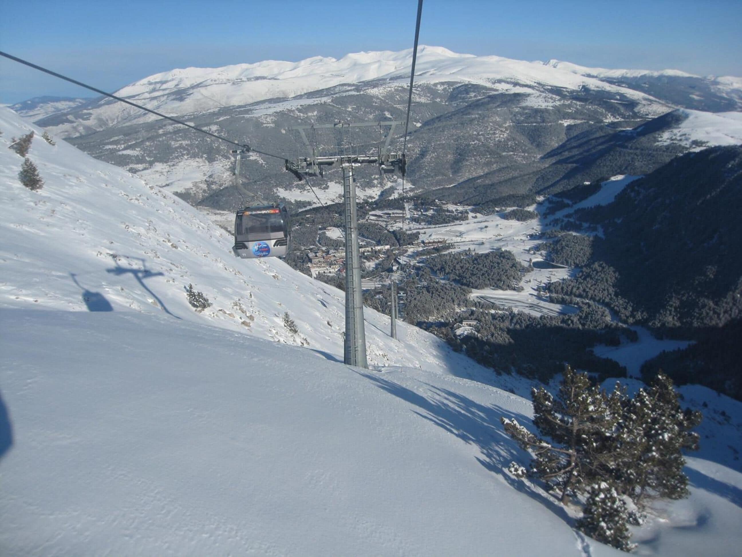 Un telesilla con sistema de cabina, una montaña nevada y un pequeño edificio en el valle.