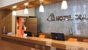 Taulell de recepció d'hotel amb superfície de fusta, tres llums penjants i paret amb textura de pedra, on es pot veure el nom de l'hotel.
