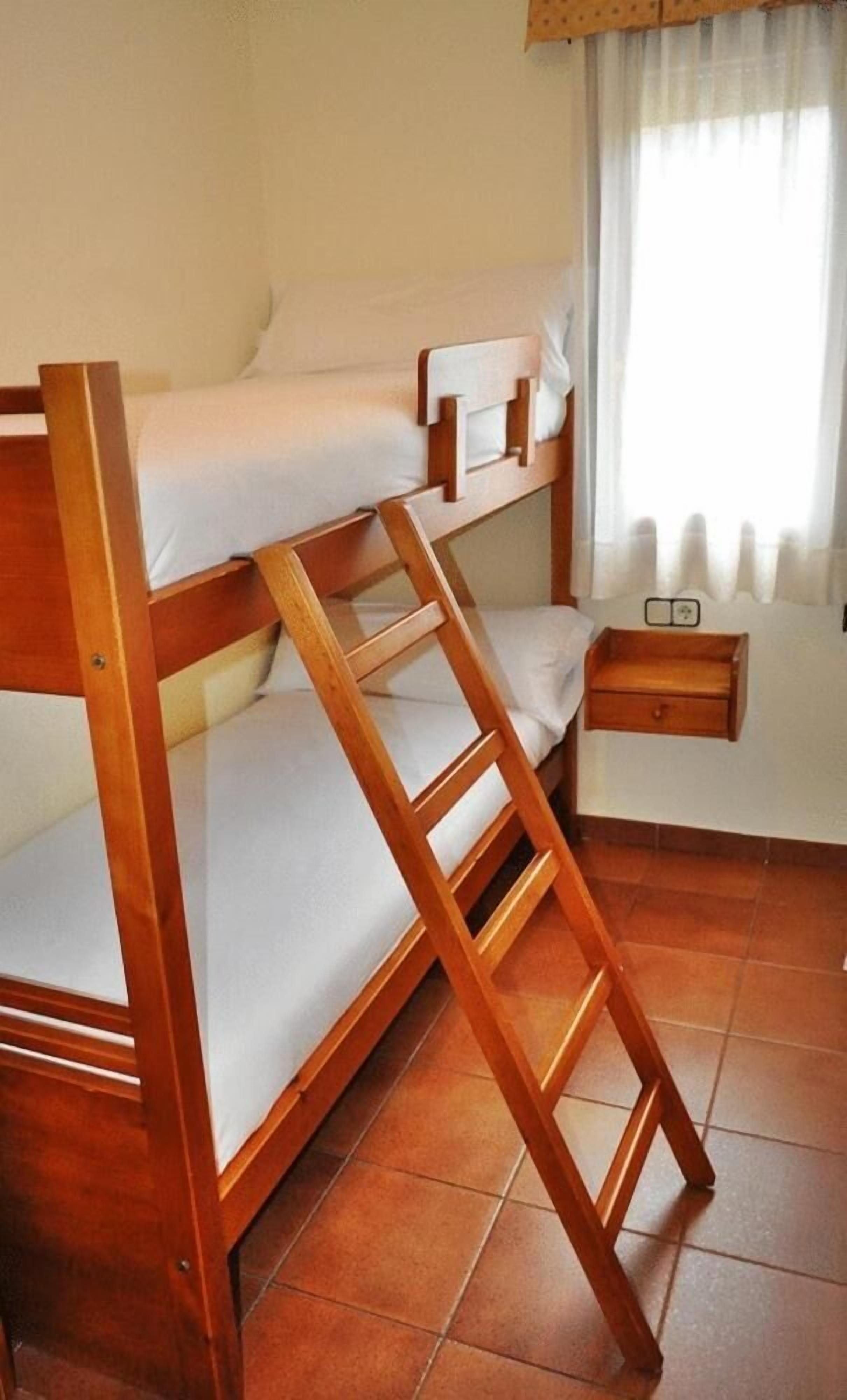 Un lit superposé avec une structure en bois et une literie blanche, une petite table de chevet et une fenêtre avec des rideaux.