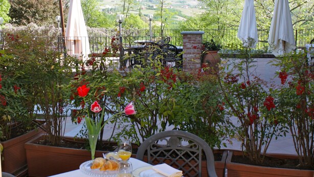 An outdoor dining area with a table set for two, surrounded by potted plants and flowers. - Villa Lauri (Neive)