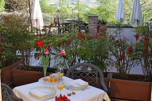 An outdoor dining area with a table set for two, surrounded by potted plants and flowers. - Villa Lauri (Neive)
