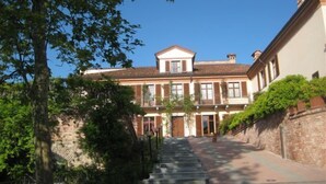 A two-story building with a central entrance, a staircase leading up to it, and a brick wall on one side. - Villa Lauri (Neive)
