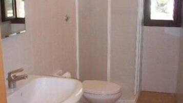 A bathroom with two toilets, a sink, and a shower enclosure.