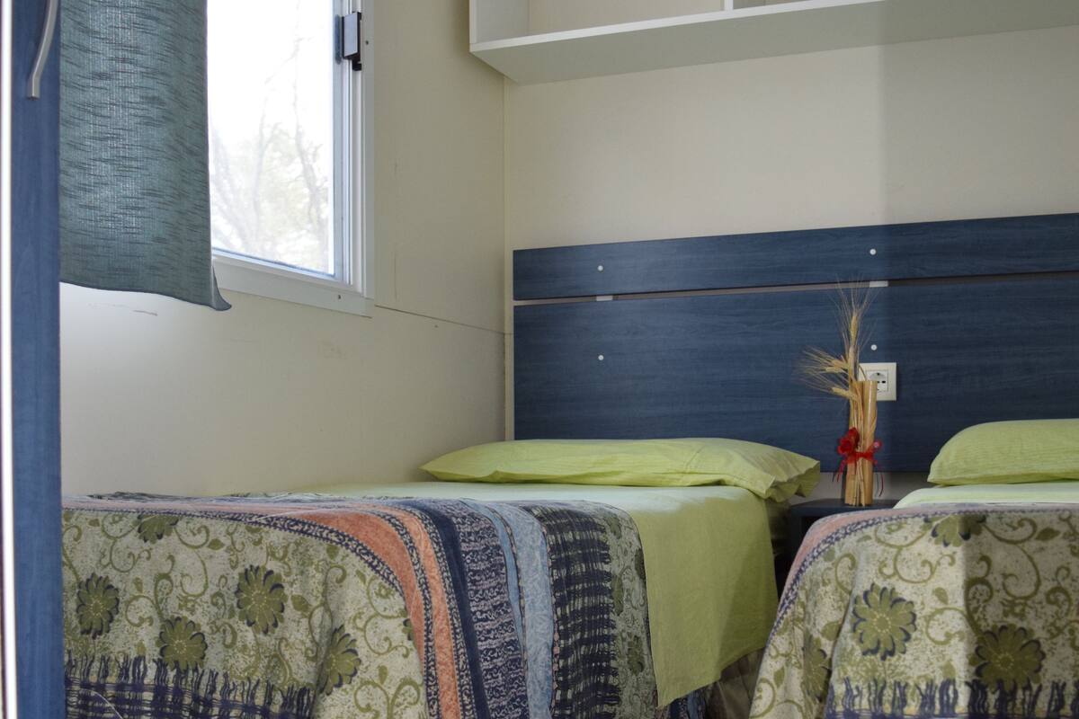 A bedroom with two beds, a window with curtains, a headboard, and a small shelf.