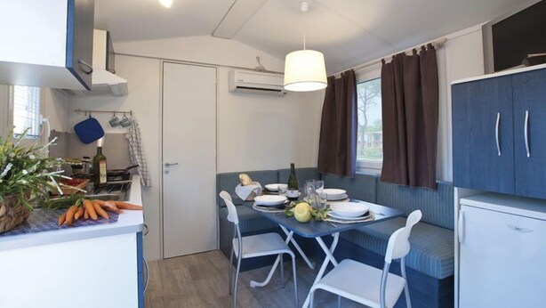 A compact kitchenette with a dining area, a built-in oven, and a window with curtains. - Villaggio Camping Bosco Selva (Alberobello)