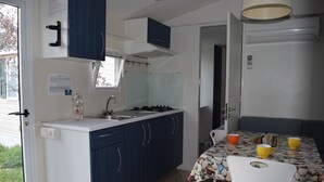 A compact kitchen with a sink, stove, and cabinets, a dining table with chairs, and a door leading to another room. - Villaggio Camping Bosco Selva (Alberobello)