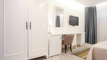 Quarto de hotel com guarda-roupa branco, escrivaninha com luminária, televisão, cadeira e cama.