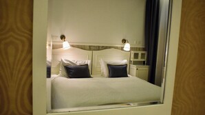 Hotellihuone, jossa on sänky, kaksi yöpöytävalaisinta, yöpöytä ja peili.