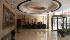 Un hall de hotel con una recepción, un cuadro grande en la pared y una entrada de cristal.