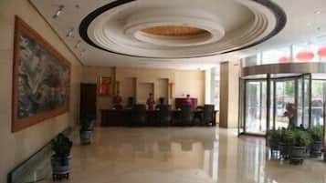Un hall de hotel con una recepción, un cuadro grande en la pared y una entrada de cristal.