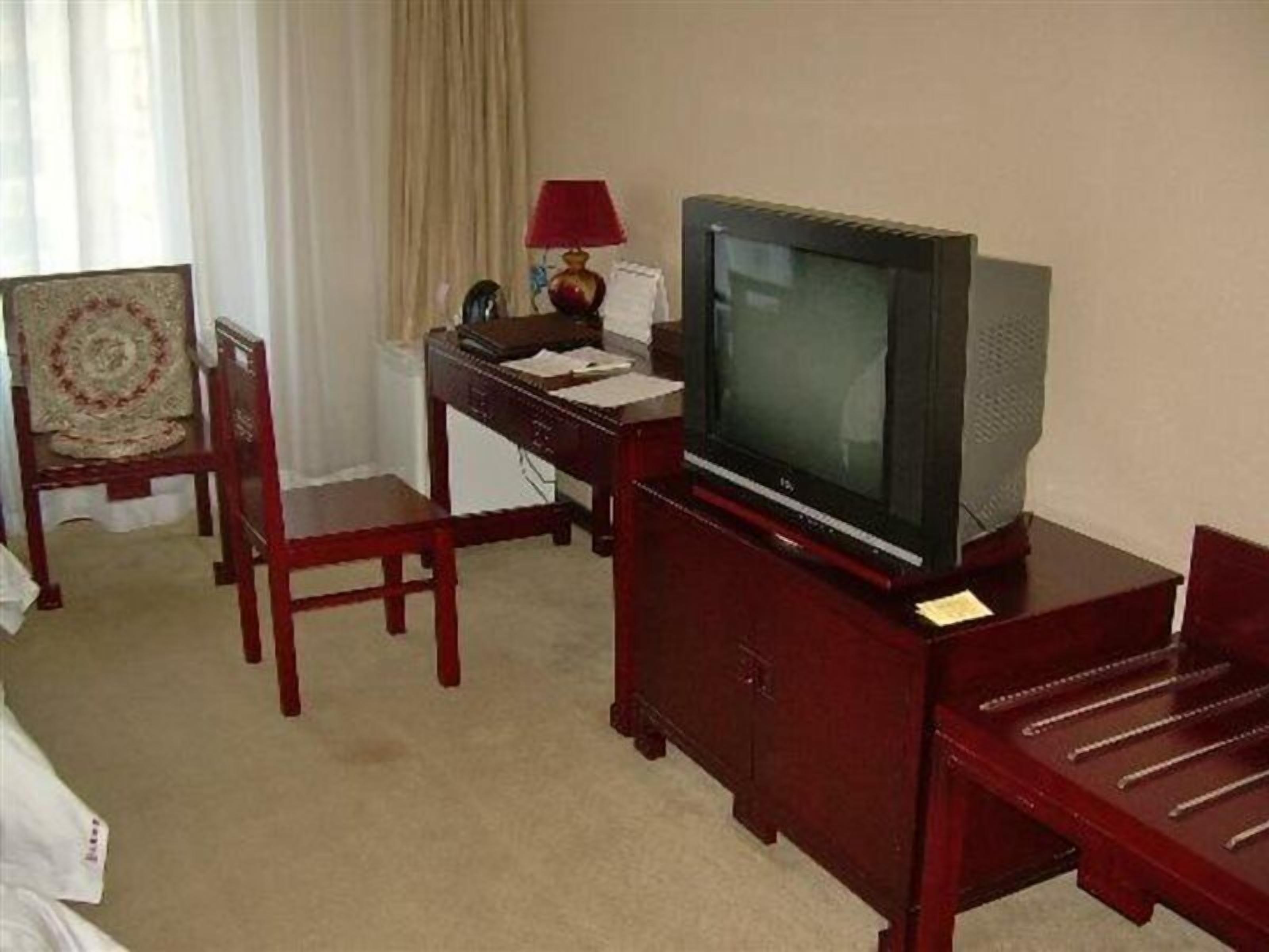Een hotelkamer met een houten bureau, een televisie, een stoel en een bed.