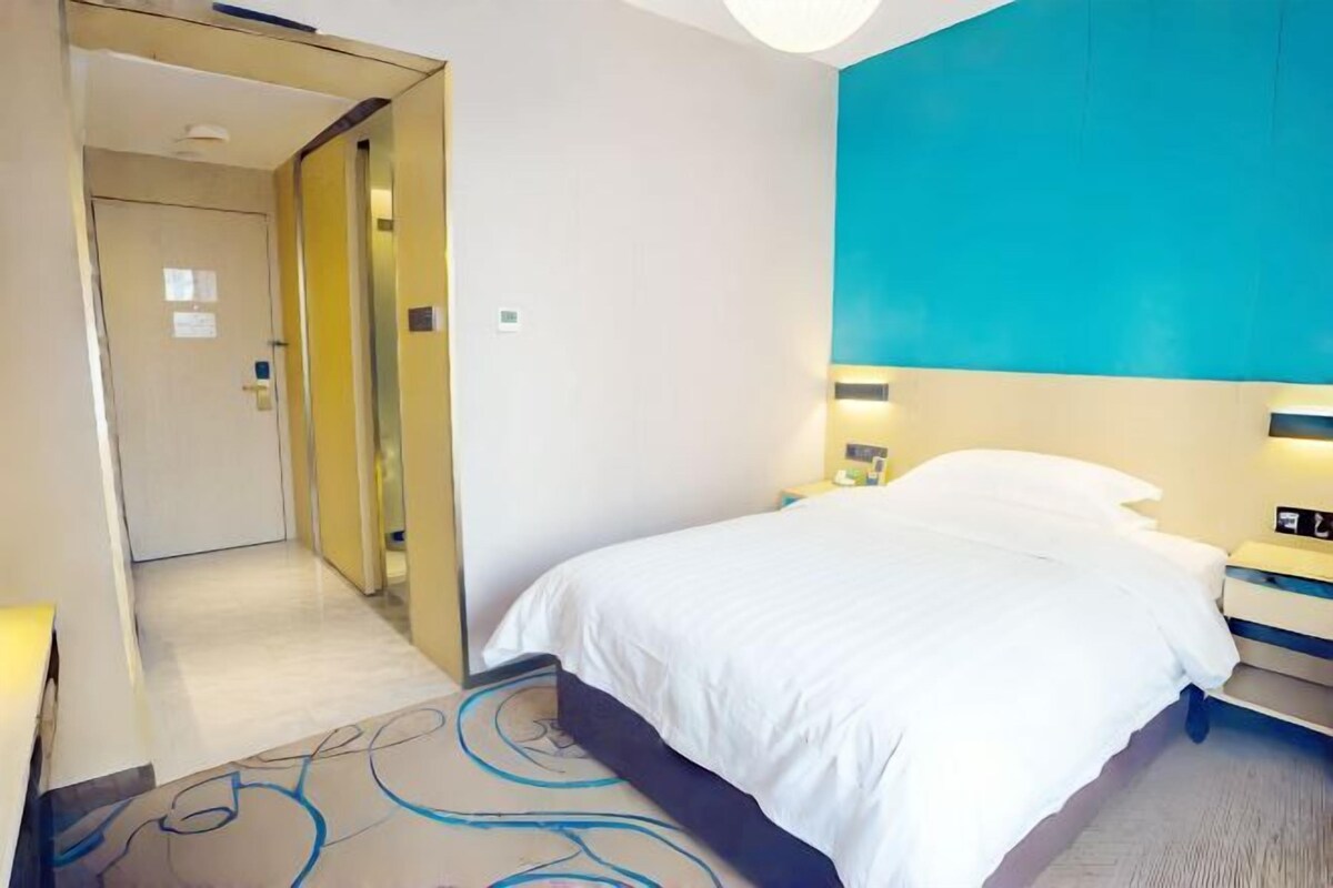 A hotel room with a bed, a nightstand, a lamp, and a door leading to another room.