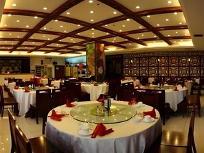 A restaurant with round tables, a high ceiling with wooden beams, and a decorative pillar. - Ruyi Business Hotel Beijing (Beijing)
