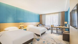 Habitación de hotel con dos camas, un escritorio, una silla, un televisor y un ventanal con cortinas.