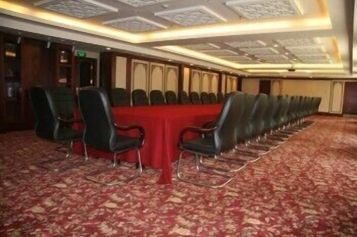 Un salón de conferencias con una larga mesa y sillas, piso alfombrado y techo con diseño.