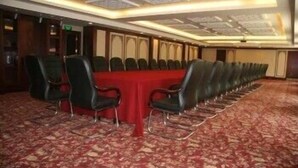 Un salón de conferencias con una larga mesa y sillas, piso alfombrado y techo con diseño.