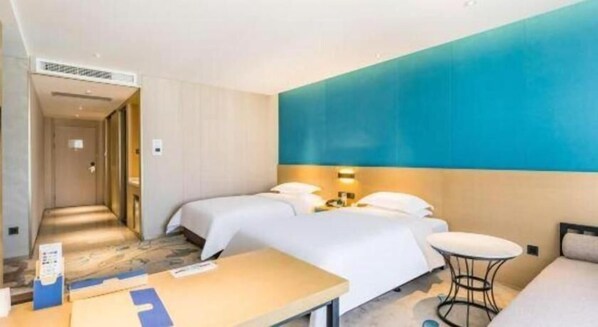 Habitación de hotel con dos camas, un escritorio, una mesita redonda y una pared decorada en tono azul.