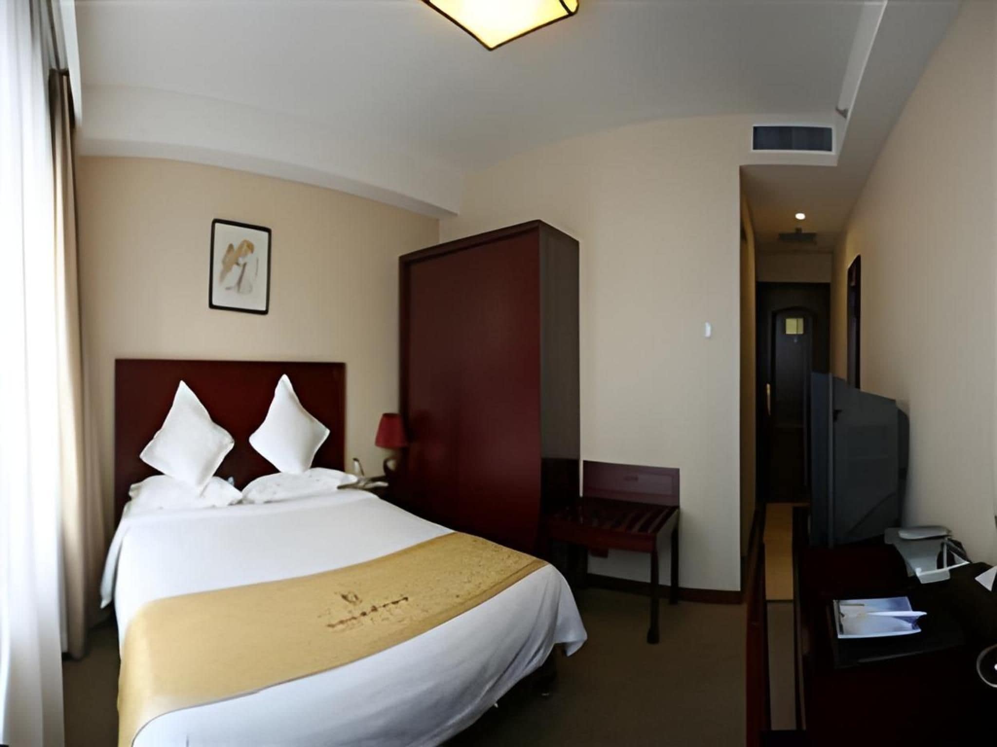 A hotel room with a bed, a desk, a chair, a television, and a door.