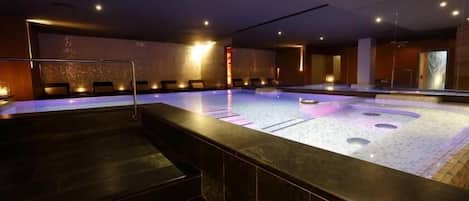 Espaço de spa com uma piscina aquecida grande, área de estar e balcão de recepção.