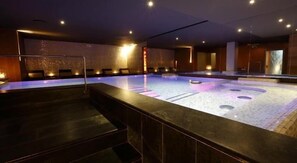 Ein Wellnessbereich mit großem, beheiztem Pool, Sitzgelegenheiten und einer Rezeption.