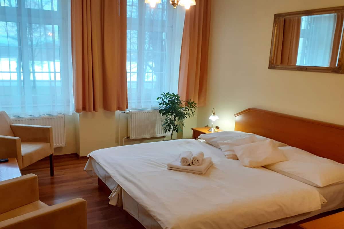 A hotel room with a bed, a chair, a desk, a lamp, and a window with curtains.