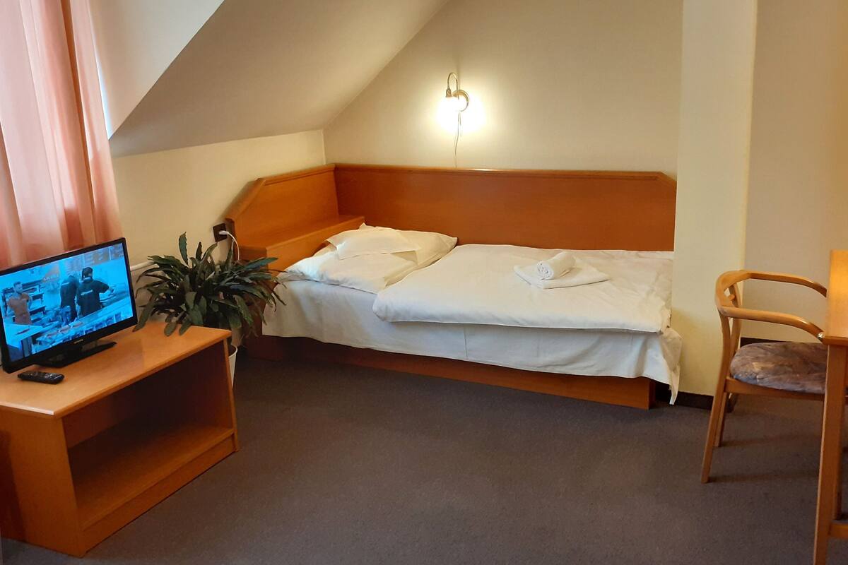 A small, cozy hotel room with a single bed, a desk, a chair, a television, and a lamp.