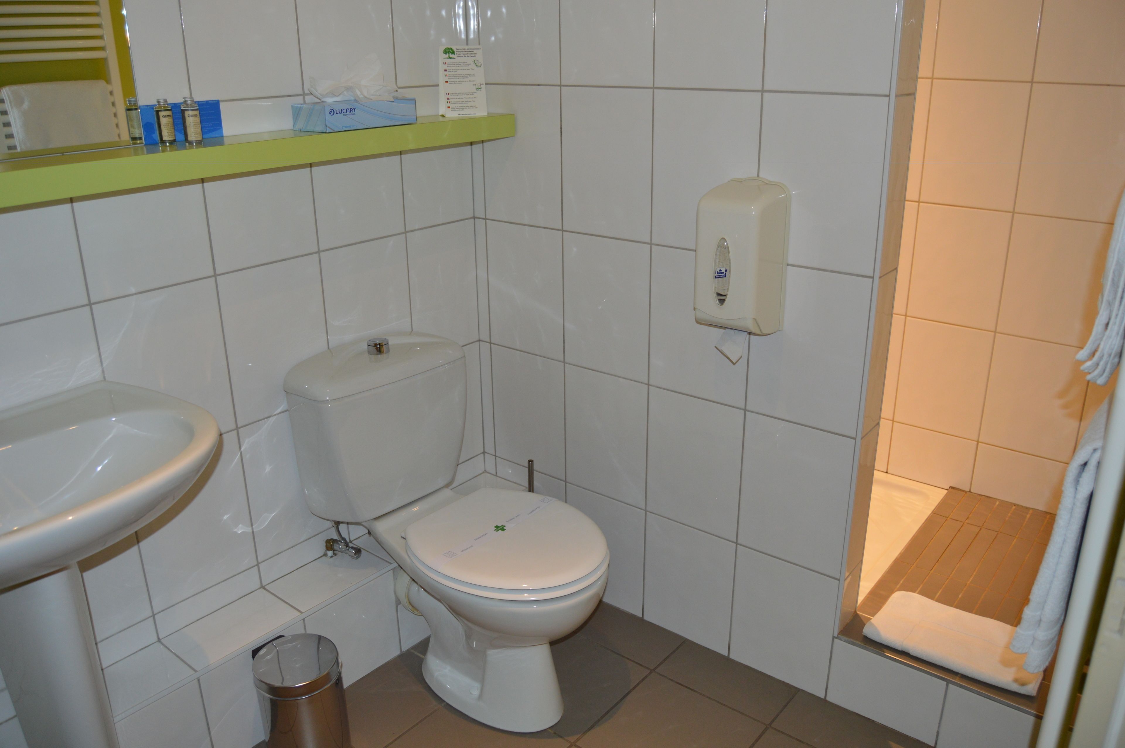 A bathroom with a toilet, sink, and a soap dispenser on the wall.