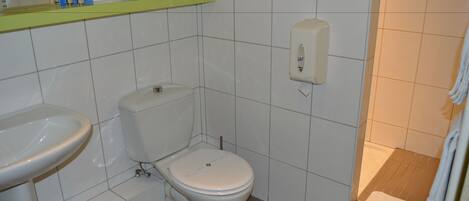 A bathroom with a toilet, sink, and a soap dispenser on the wall.