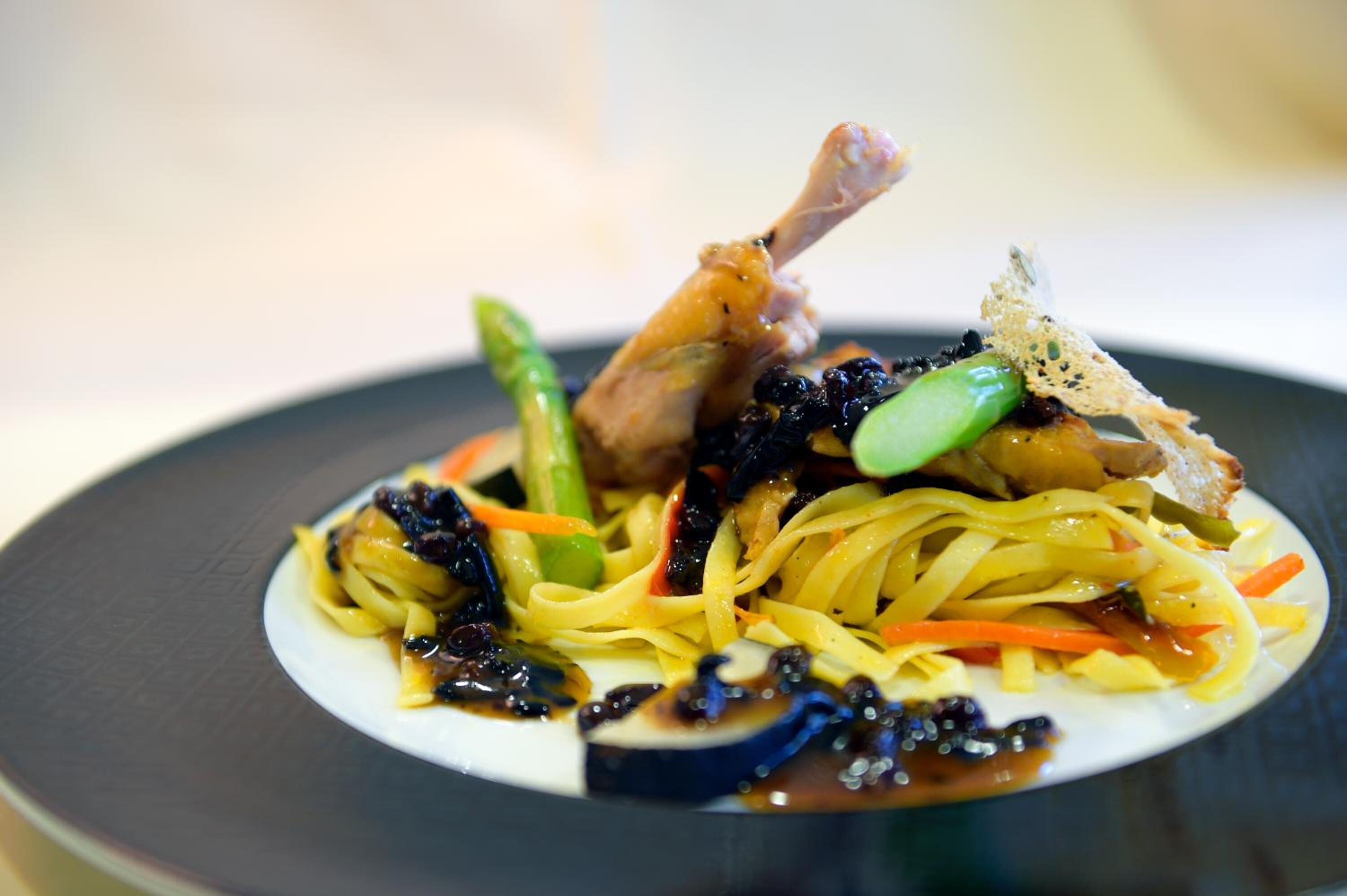 Un plato de comida con fideos, verduras y un trozo de carne.