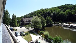A riverside view with a building, parked cars, and a dining area with umbrellas. - Hôtel du Lac (Guebwiller)